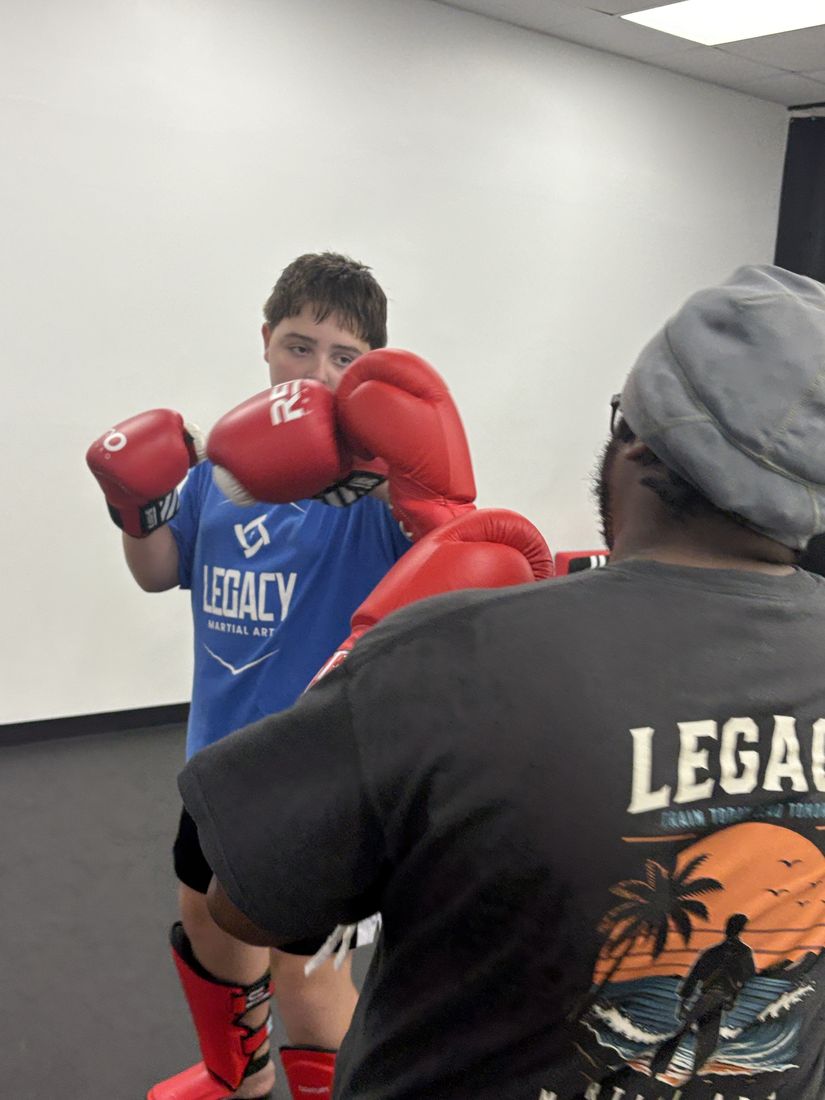 A teenage student in Legacy Martial Arts gear working pads with an instructor